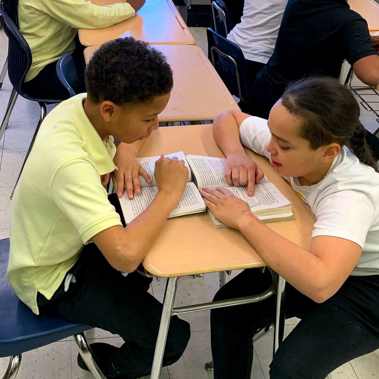 Two Roberto Clemente Middle School students read and discuss a book together during a classroom lesson.